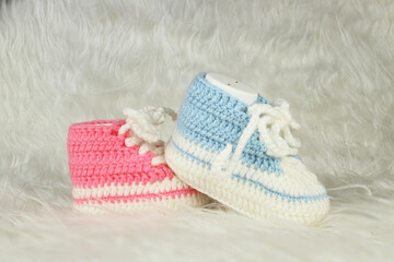 Knitted pink and blue booties on white fluffy blanket. Gender party concept idea. Booties for baby girl or boy for first step. 