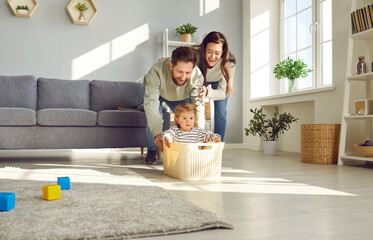 Young happy family having fun in the living room at home together with their child riding her in...