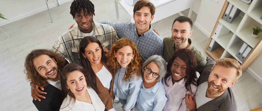 Happy diverse business team at work in office. Top view high angle shot from above group portrait of young and senior multiracial multiethnic people standing together, looking up at camera and smiling