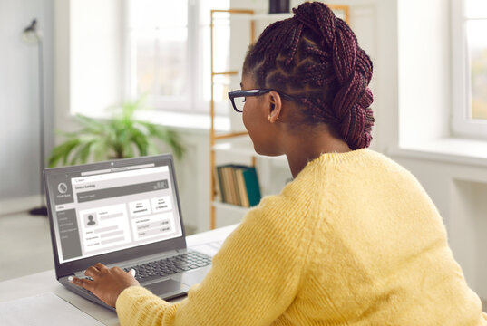 Young African American Woman With Beautiful Afro Braids Sitting At Desk At Home, Using Laptop Computer, Browsing Online Banking Website, Visiting Business Account Page, And Updating Personal Details