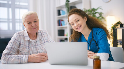 Portrait of smiling nurse and mature woman sitting with a laptop at home