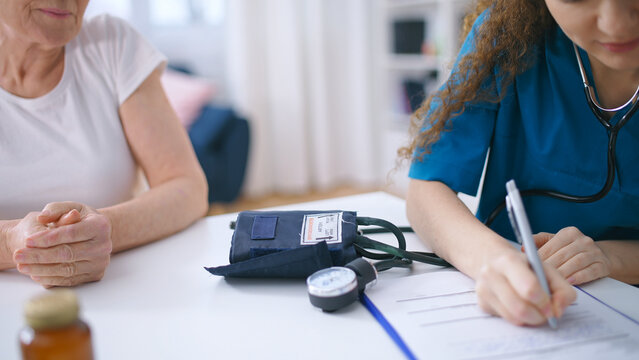 Physician checking old female patient blood pressure and writing down results