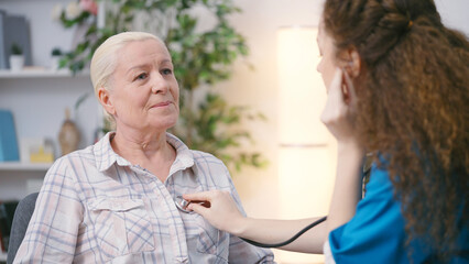 Woman therapist listening to heartbeat of a senior woman, health check-up