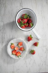 Vertical top view of a plate and metal sieve with juicy red strawberries on a marble table