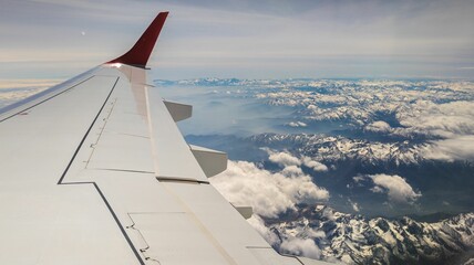 Airplane window view of a mountain range covered with snow and clouds