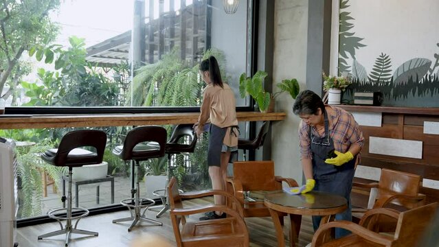 Elderly Asian mother standing cleaning, coffee shop with daughter, cafe owner's daughter is closing cafe in evening when it is open all day, mother daughter help clean up prepare for opening next day.