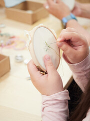 child's hands with needle and thread embroidering fabric on a stretcher frame