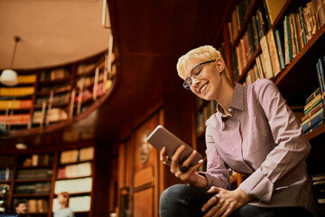 Young smiling caucasian woman with short hair using a smart phone in a library
