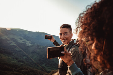 Young female couple taking a picture of the sun setting while out hiking in the mountains