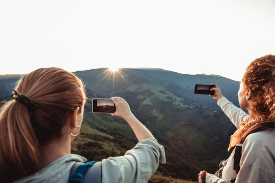 Young female couple taking a picture of the sun setting while out hiking in the mountains