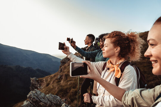 Young and diverse group of female friends taking a picture of a view with their smart phones while hiking in the mountains and hills