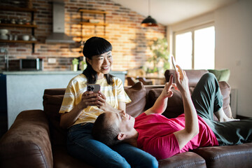Young female lesbian couple using a smart phone while sitting on the couch in the living room
