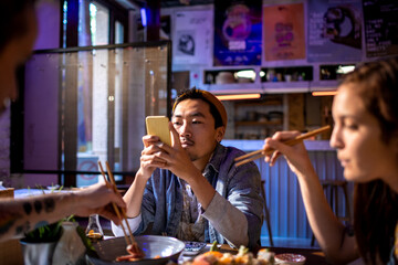 Diverse group of young people eating sushi and using a smart phone in a sushi restaurant