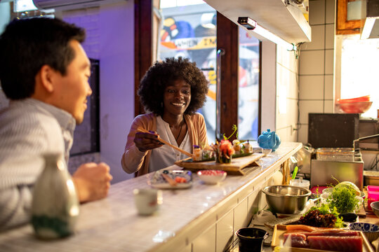 Young asian man and a african woman having a romantic date in a sushi restaurant bar