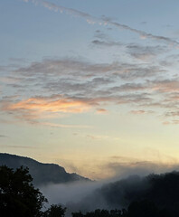 Clouds hang over mountain silhouettes at sunrise or sunset 