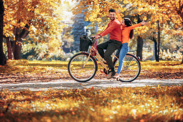 Happy young couple riding a bicycle on a sunny autumn day. The park is colorful