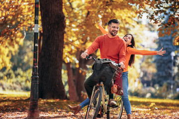 Happy young couple riding a bicycle on a sunny autumn day. The park is colorful