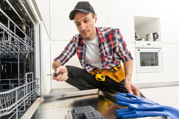 Young African Repairman Fixing Dishwasher In Kitchen