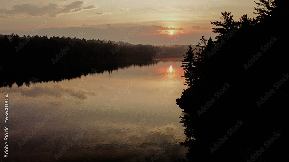 Poster Tranquil lake scene with majestic pine trees silhouetted against a golden sky at sunset