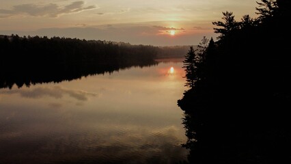 Tranquil lake scene with majestic pine trees silhouetted against a golden sky at sunset