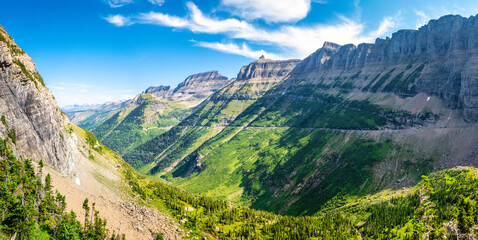 View of Logan creek valley in Glacier National Park, Montana with Pollock mountain (right), Bishop Cap, Mount Gould and Haystack Butte, Going-To-The-Sun road (middle), slopes of Mount Oberlin (left) - obrazy, fototapety, plakaty