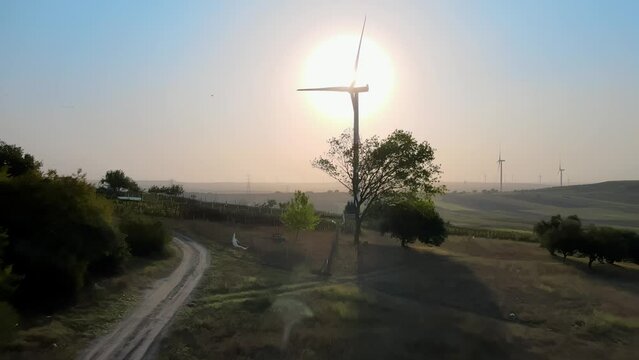 Drone shot over of green fields and windmills against sunrise