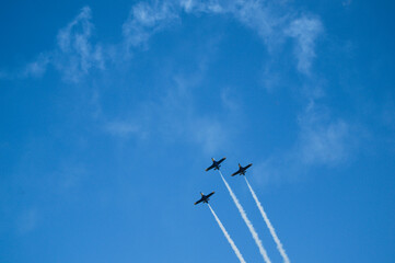 three planes synchronously fly up and leave a trail with a blue sky in the background
