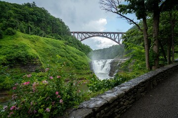 Fototapeta premium Scenic view of a bridge crossing a waterfall with a lush green forest in Letchworth State Park