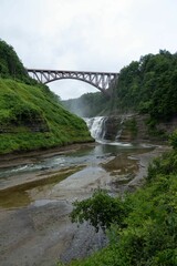 Scenic view of a bridge crossing a waterfall with a lush green forest in Letchworth State Park