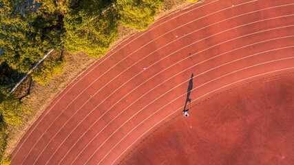 Aerial view of a person running on a running track with the sun casting a golden light on the path
