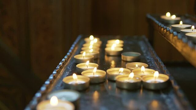 Candles in the church left by parishioners. Christians pray for the health and repose of their loved ones and relatives. Church mass. Round metal candles. Lighting a candle in front of saints and icon