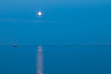 Luna piena che si riflette sulla calma superficie del mare con bricole per le barche.