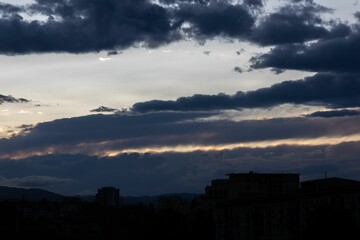 Fototapeta premium Scenic view of silhouettes of buildings against a cloudy evening sky lit by the setting sun