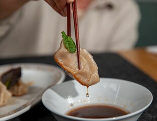 Close-up of a woman dunking a dumpling into a sauce