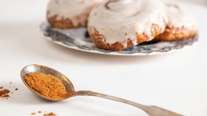 Close-up image of two Cinnabon cinnamon rolls on plates, with a spoon of cinnamon powder on the side
