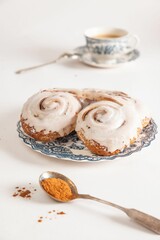 glazed cinnamon rolls sit on a plate with a spoon and tea cup in the background