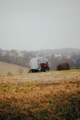 Fototapeta premium Tractor covered with a weatherproof cover near a hay bale on a misty day