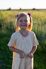 A little charming girl smiles broadly, walks around the field, sunset
