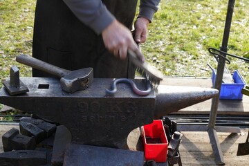 Male blacksmith shaping a piece of glowing iron, using a hammer and steel brush, on a sunny day