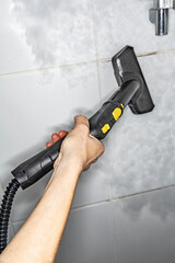 Woman washing ceramic tiles in the bathroom with a steam generator