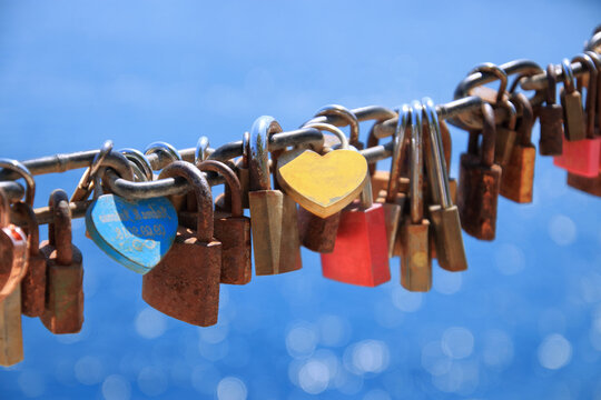 Close up of old rusty love locks on chain against background of blue sea on sunny day. Close up of old rusty love locks on chain against background of blue sea on sunny day. Trip for valentines day  - Powered by Adobe