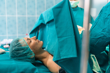 Closeup of female patient under anesthesia with protective cap having breast surgery in private...