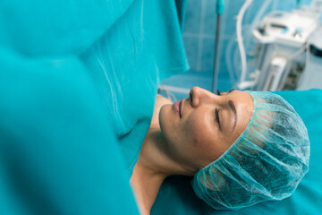 Portrait of adult woman patient with eyes closed sleeping under anesthesia with medical sheets on...