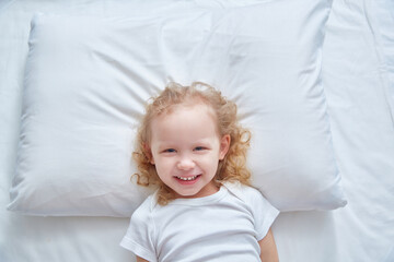 Smiling cute girl on a white pillow. Copy space