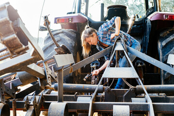 Young female mechanic repairing tractor at field