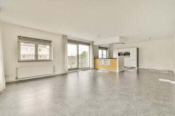 an empty living room with white walls and grey flooring, there is a large window looking out onto the street