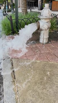 Vertical video shows water gushing out of an open fire hydrant, flooding a city street.