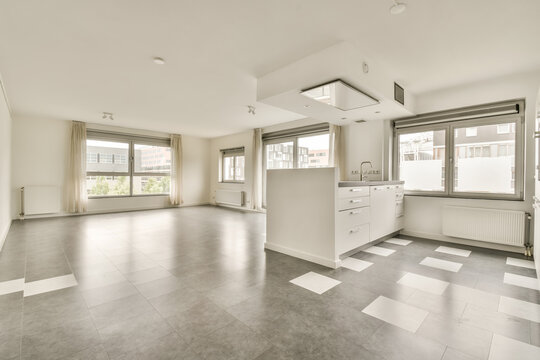 an empty living room with white walls and grey flooring, there is no one in the photo to be seen