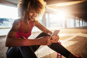 Young woman using a smart phone after jogging and exercising in a parking lot