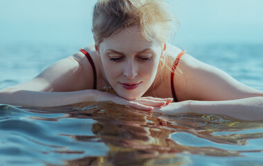 Beautiful blond young woman looking at her reflection in the water - obrazy, fototapety, plakaty